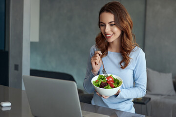 Girl eating salad and watching on laptop at home