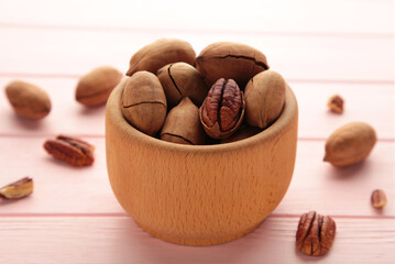 Fresh tasty pecan nuts on wooden bowl on a pink background. Whole and cracked pecans.
