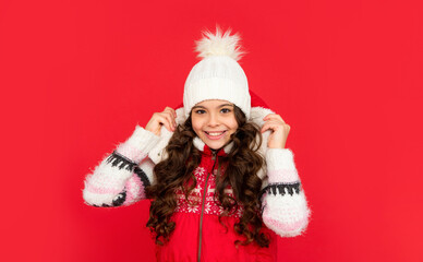 stylish emotional kid with curly hair in christmas waistcoat and hat. teen girl on red background.