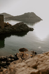 Relaxing scene at a holiday lounge deck by the sea overlooking blue waves and ocean, sun reflecting in water, blue sky and rocks in the background