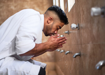 A young Muslim man performs wudu during prayers at a mosque by cleansing his face in the washroom