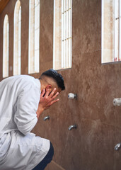 A young Muslim man performs wudu during prayers at a mosque by cleansing his ears in the washroom