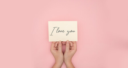 Top view of woman female hands holding a paper message with the text I love you, isolated on pink background
