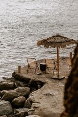 Relaxing scene at a holiday lounge deck by the sea overlooking blue waves and ocean, sun reflecting in water, blue sky and rocks in the background