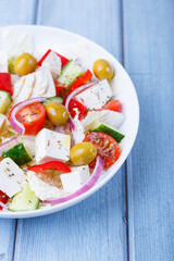 Greek salad. Traditional Greek dish. Healthy vegetarian food. Fresh vegetables and feta cheese in a white plate. Close-up, blue background.