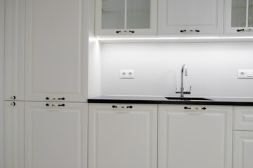 Modern and elegant kitchen with white drawers and cupboards, black marble countertop and built-in sink with silver tap