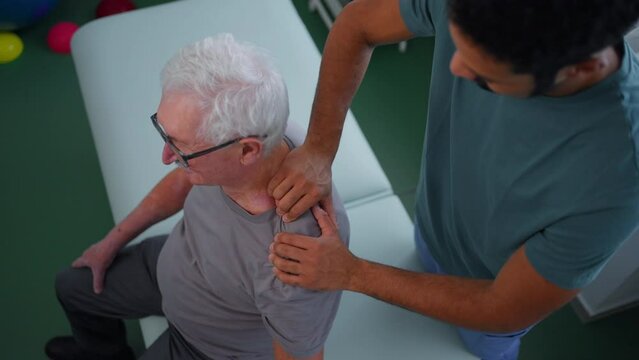 High angle view of young physiotherapist massaging the shoulder of senior patient in a physic room