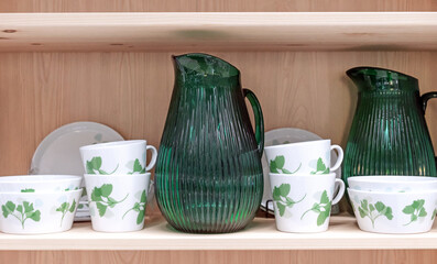 Green glass jug and ceramic cups with green ornaments on the kitchen shelf.