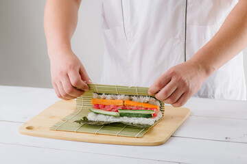 the chef cook prepares sushi and wraps a letter to the nori in the roll, on white background