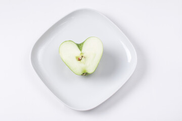 a green apple on a white plate in the shape of a heart. Valentine's Day, congratulations on the holiday
