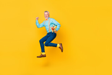 Photo of excited hurrying retired man wear turquoise shirt suspenders running jumping bouquet isolated yellow color background
