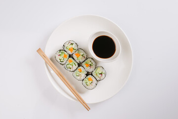 Sushi with chopsticks on a white plate. Sushi roll japanese food in restaurant isolated on white background. Fresh hosomaki pieces with rice and nori.