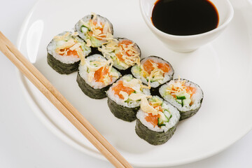 Sushi with chopsticks on a white plate. Sushi roll japanese food in restaurant isolated on white background. Fresh hosomaki pieces with rice and nori.