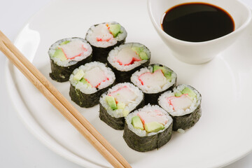 Sushi with chopsticks on a white plate. Sushi roll japanese food in restaurant isolated on white background. Fresh hosomaki pieces with rice and nori.