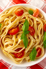 Pasta with tomato slices and basil leaves. The plate is on a checkered napkin
