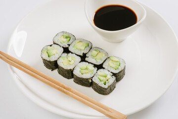Sushi with chopsticks on a white plate. Sushi roll japanese food in restaurant isolated on white background. Fresh hosomaki pieces with rice and nori.