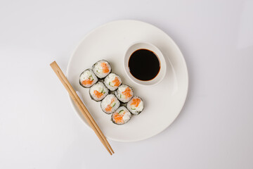 Sushi with chopsticks on a white plate. Sushi roll japanese food in restaurant isolated on white background. Fresh hosomaki pieces with rice and nori.