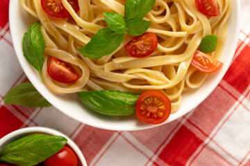 Pasta with tomato slices and basil leaves. The plate is on a checkered napkin