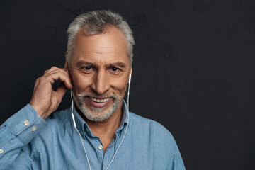 Smiling mature man listening music in earphones