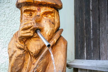The figure is carved from wood. Grandfather made of wood with a straw in his mouth pours water