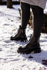 Woman in fashionable black boots on white snow, close up. Women's legs in stylish winter leather boots