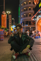 Obraz na płótnie Canvas Portrait of young stylish brunet caucasian man in black leather jacket and yellow sunglasses Sitting on the street at night. High quality photo