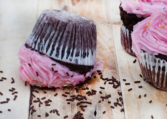 cupcake with pink frosting fallen upside down with messed chocolate sprinkles .