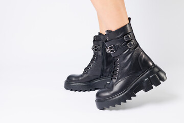 Legs of a woman in black leather boots from a new collection on a white background, legs of a girl in fashionable leather boots spring 2022.