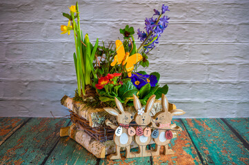 Flower arrangement with wooden Easter bunnies as decoration and the text Easter on the Easter eggs.