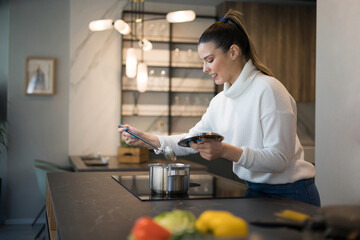 Fototapeta premium A beautiful young woman looking at the soup she is cooking. Healthy life style.