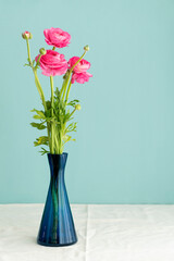 Lush natural light old Dutch Delft blue lidded vase with pink ranunculus on white linen against a blue background