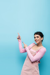 young brunette woman in pastel clothing pointing with fingers and looking at camera isolated on blue