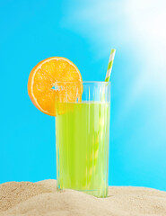 Summer drink in a glass with a piece of orange on the sand.