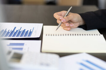 Fototapeta premium Businesswoman working on her desk holding a pen and writing a note on a notepad.