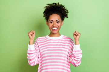 Photo of lucky sweet woman wear striped sweater smiling rising fists isolated green color background