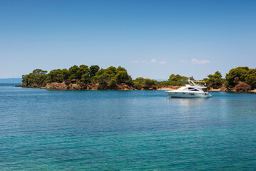 Panoramic photo of the turquoise sea with a white yacht docked in the  bay on a summer day in Greece
