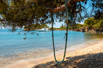 Rope swing on a tree on a beach with a lagoon and a moored yacht in the background