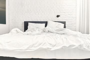 An unmade double bed in a modern, white loft-like room