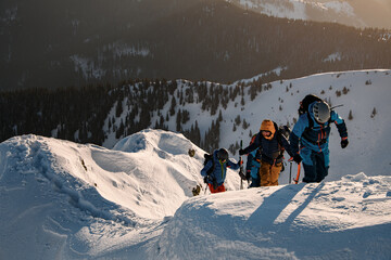 group of skiers in bright ski suits climbing up at snow-covered mountain trail