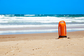 Lifeguard rescue can on the beach. Orange rescue buoy in vertical position on the sand. - Powered by Adobe
