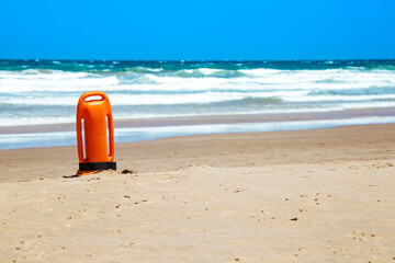 Lifeguard rescue can on the beach. Orange rescue buoy in vertical position on the sand.