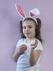 A cute little girl in a white T-shirt and with hare ears smiles, holds colored Easter eggs in her hands, presses them to herself. Easter concept.