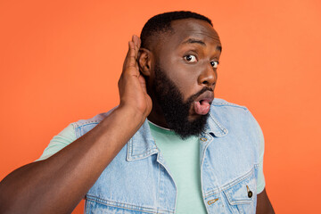 Photo of shocked african guy dressed jeans waistcoat arm ear listening you isolated orange color...