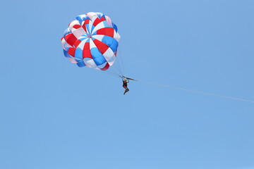 A woman is gliding using a parachute on the background of cloudy blue sky.