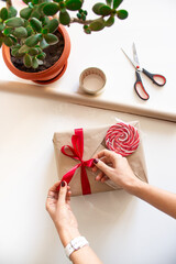 The girl's hands tie a red ribbon bow and decorate a gift for the holiday. Gift wrap. Kraft paper...