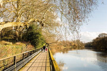 Passage aménagé en bois au-dessus et au bord d'une rivière tranquille avec personnages, femme et...