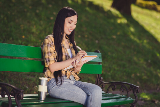 Photo of charming sweet young woman dressed plaid shirt sitting bench writing planner to do list smiling outside countryside nature