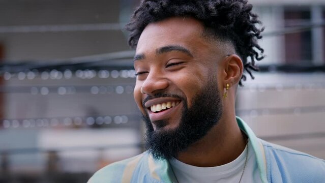 A happy young Brazilian man standing outside in drizzle smiling at camera