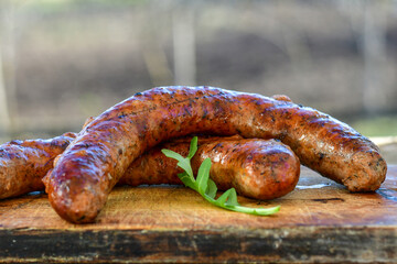 Fototapeta premium Grilled pork juicy sausages on wooden board outdoors. Grilling food, bbq, barbecue, picnic