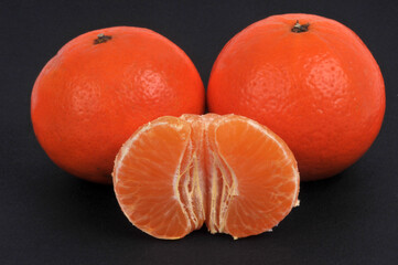 Mandarines entières et mandarine épluchée en gros plan sur fond noir